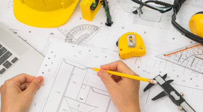 hand-over-construction-plans-with-yellow-helmet-and-drawing-tool